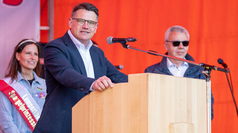 Ministerpräsident Rhein am Rednerpult bei der Spargelwanderung, hinter ihm die Lampertheimer Spargelprinzessin.