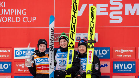 Siegerinnen des Damen-Springen stehen auf Siegertreppe, halten Pokale uns Ski