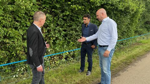 Landwirtschaftsminister Jung steht gemeinsam mit zwei weiteren Männern an einem Straßenrand neben dem errichteten Elektrozaun.