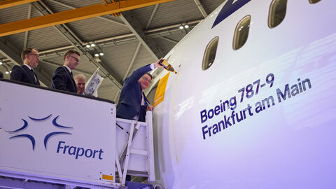 Ein Mann steht an einem Flugzeug und schüttet Sekt auf die Seite.