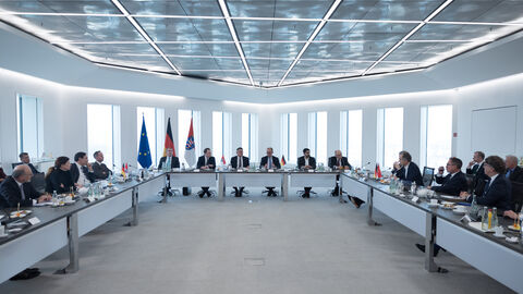 In einem Hochhaus stehen Tische in einer U-Form, wo Menschen dran sitzen.