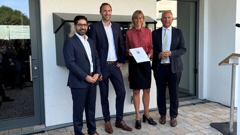 Wirtschaftsminister Kaweh Mansoori, Dr. Axel Tausendpfund (Vorstand des Verbands der Südwestdeutschen Wohnungswirtschaft, VdW südwest), Mirja Dorny (Geschäftsführerin Baugesellschaft Hanau), Innenminister Roman Poseck (v. l. n. r.) stehen nebeneinander vor einem Haus.