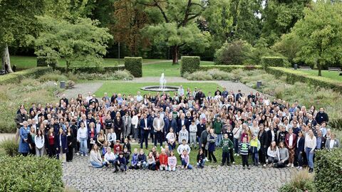 Weitwinkelaufnahme einer großen Gruppe von über hundert Personen in einem Park, alle stehen zusammen und blicken in die Kamera.